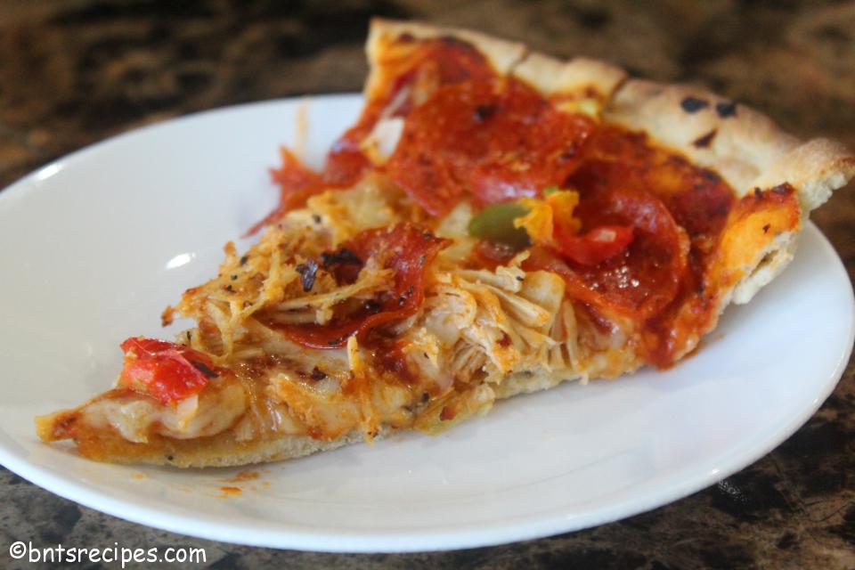 slice of homemade thin-crust cast iron skillet pizza with pepperoni bell peppers and shredded chicken facing left on white plate on granite countertop