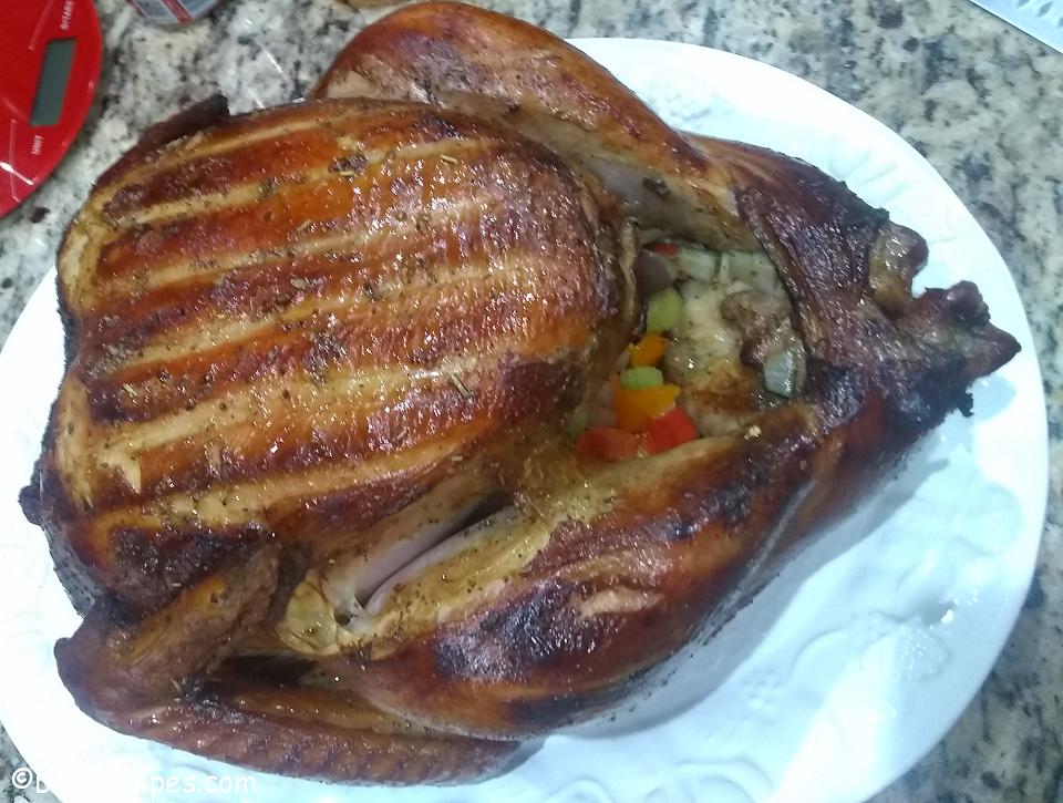 close-up of brined and barbequed turkey with onions and peppers inside on a large white serving plate on top of a granite counter with a red food scale nearby
