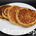 golden brown pancakes for two on a white plate with black background