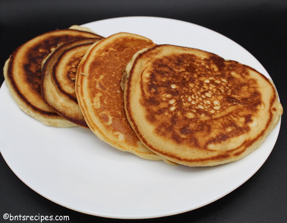 golden brown pancakes for two on a white plate with black background