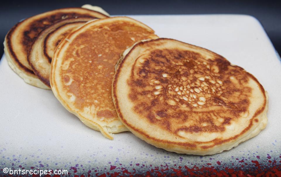 golden brown fluffy pancakes for two on a multi-colored plate with black background