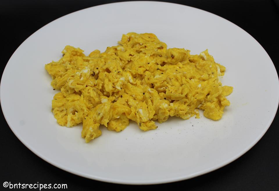close-up of cheesy scrambled eggs on a white plate with black background