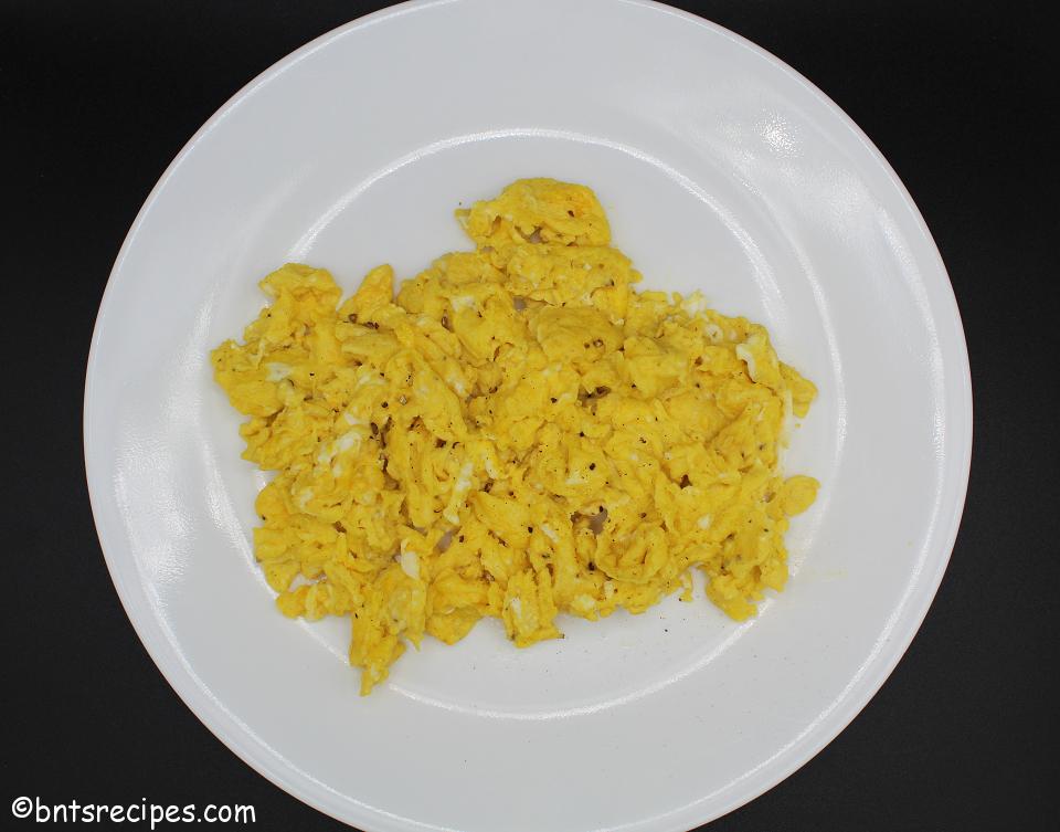 aerial view of cheesy scrambled eggs on a white plate with black background