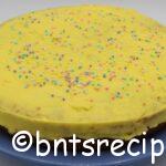 whole round yellow cake with yellow icing and pastel sprinkles on blue plate
