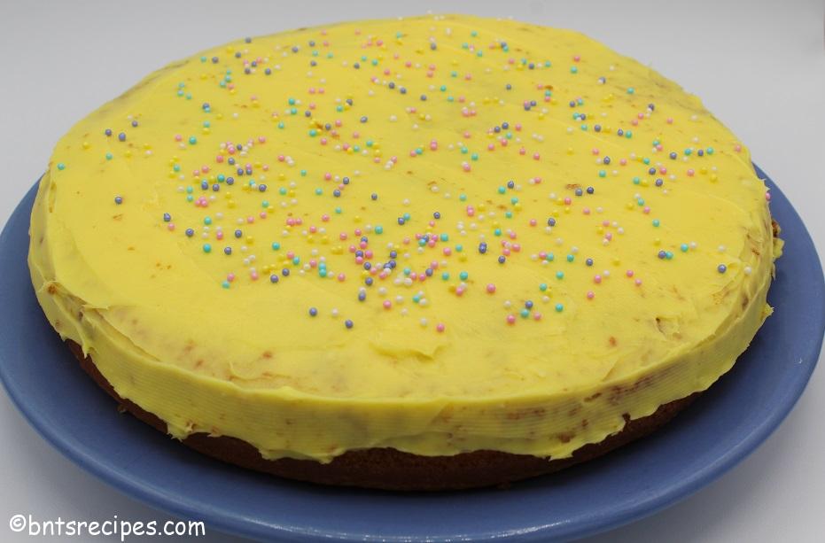 whole round yellow cake with yellow icing and pastel sprinkles on blue plate