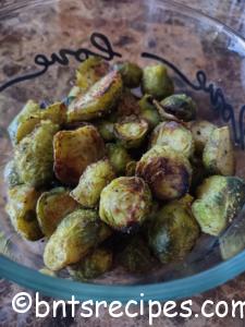 close-up of roasted brussels sprouts with a little char on them in a glass bowl that says love on it