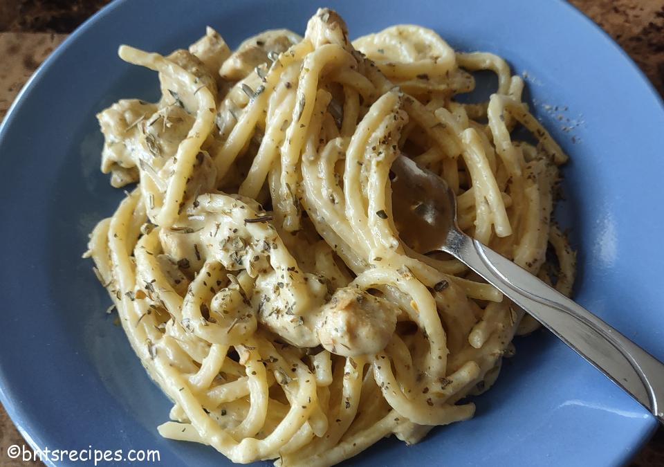close-up of cajun chicken alfredo on a blue plate with a silver fork atop a granite counter