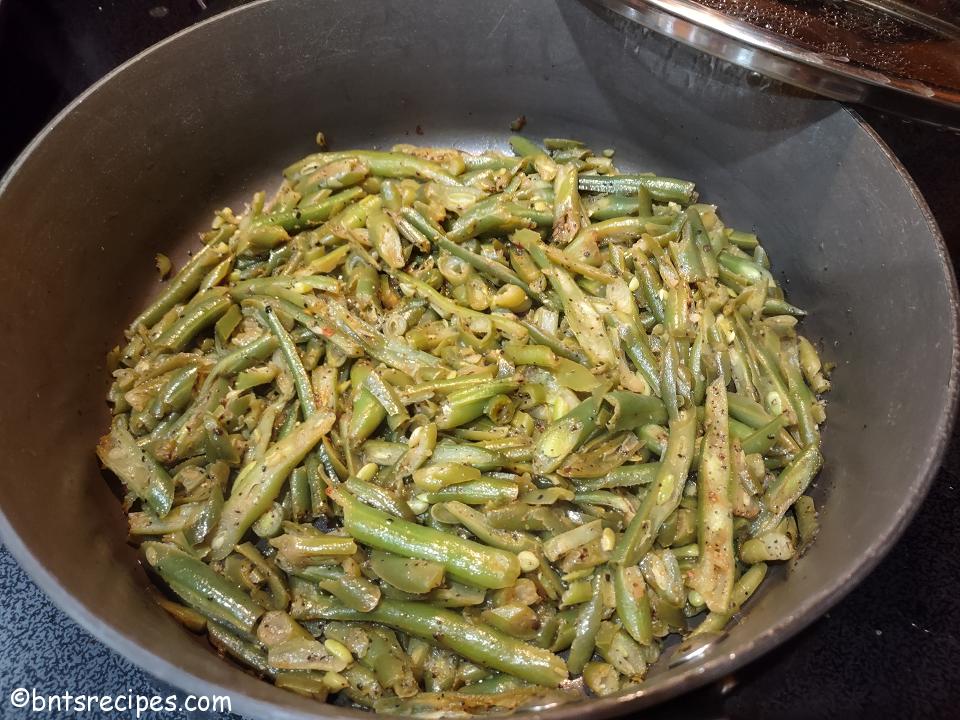 frozen french style green beans sauteed in a pan with a lid leaning on it