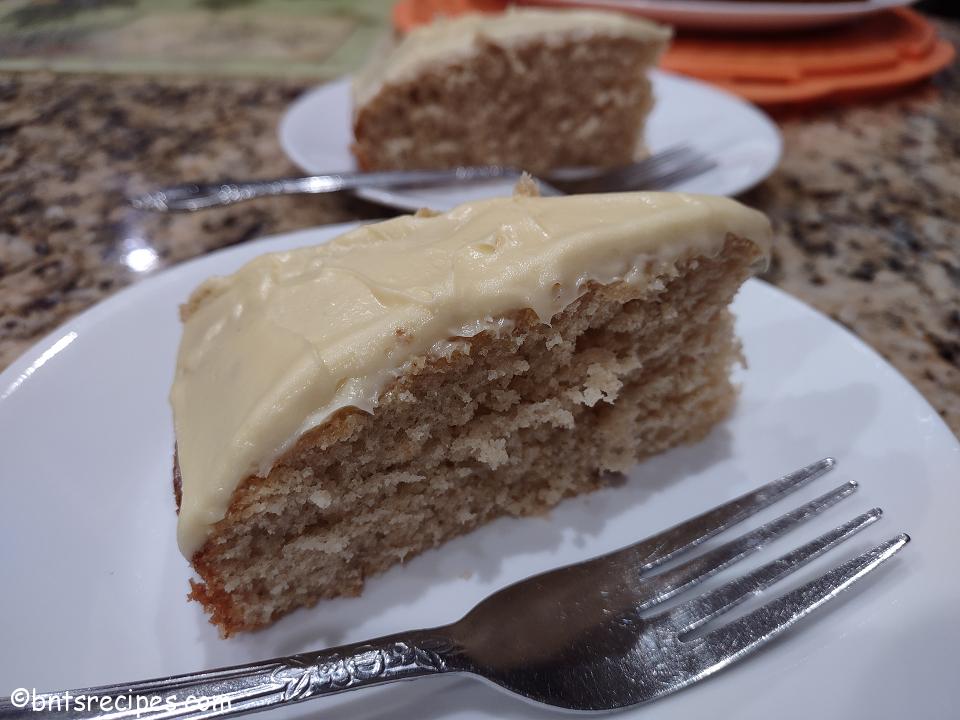 close-up of two slices of homemade grown-up yellow cake with buttercream frosting on white plates and orange cake pan on top of a granite countertop