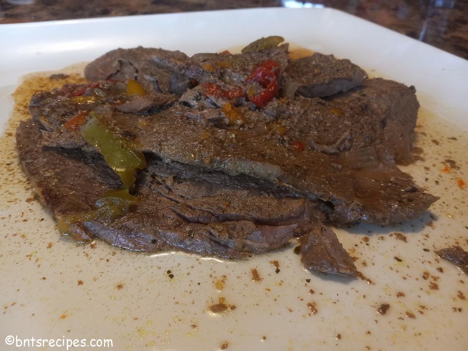 juicy and tender steak cooked in a crockpot on a white plate with bell peppers