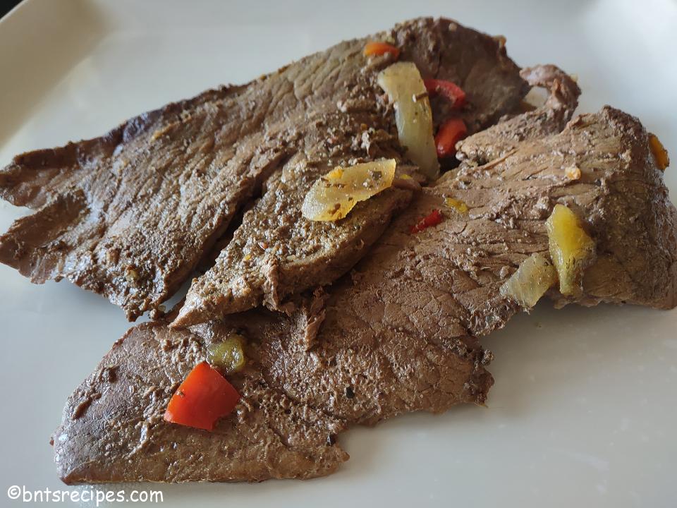 close-up of juicy and tender steak cooked in a crockpot on a white plate with bell peppers