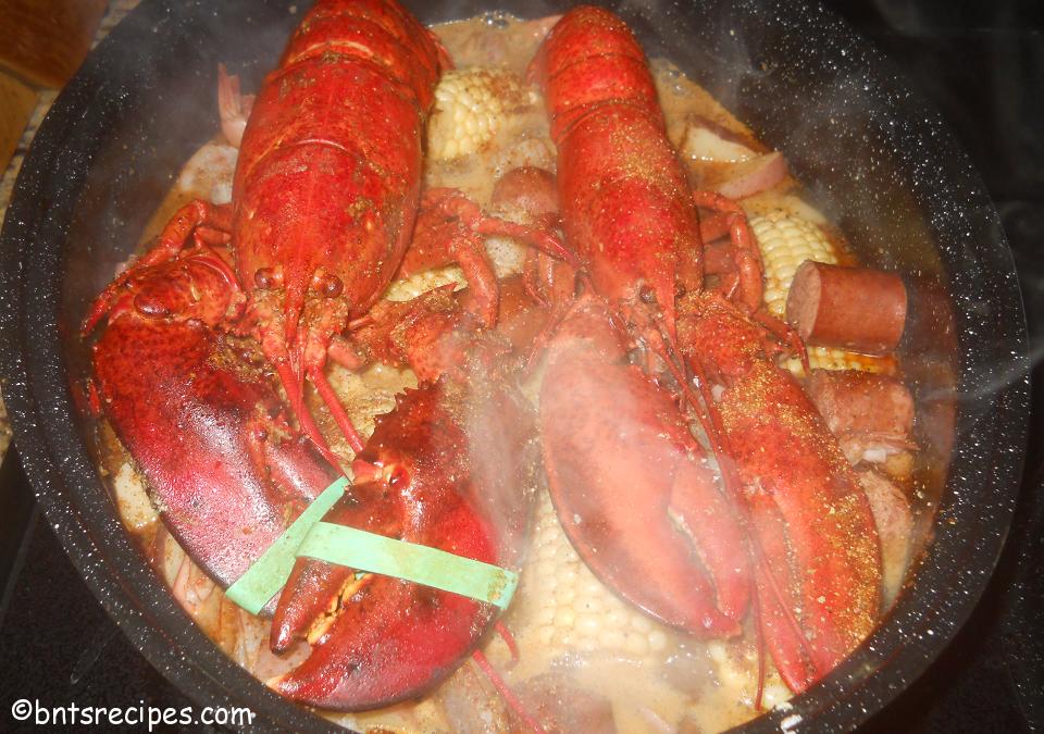 steamy whole lobsters on top of plethora of sausage corn shrimp and potatoes for seafood steam bake
