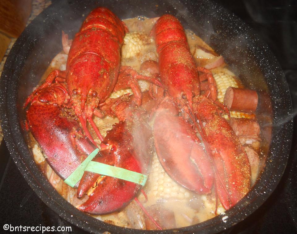 steamy whole lobsters on top of plethora of sausage corn shrimp and potatoes for seafood steam bake