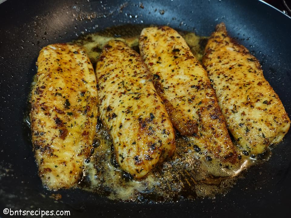 front view of no-shell taco-flavored tilapia searing in a pan with butter and oil