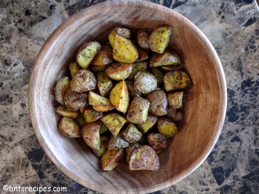 aerial view of a wooden bowl of roasted red baby potatoes with herbs and spices