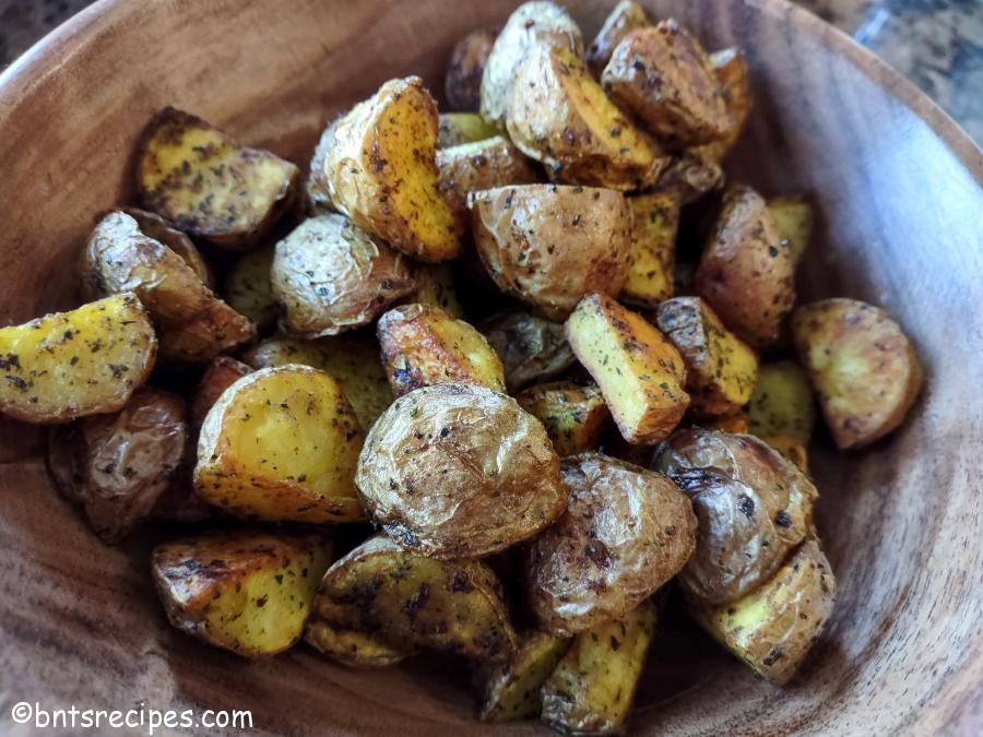 a wooden bowl of roasted red baby potatoes with herbs and spices