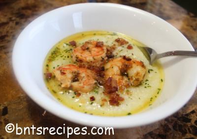 glowing bowl of creole shrimp and grits with butter bacon bits and parsley on granite counter