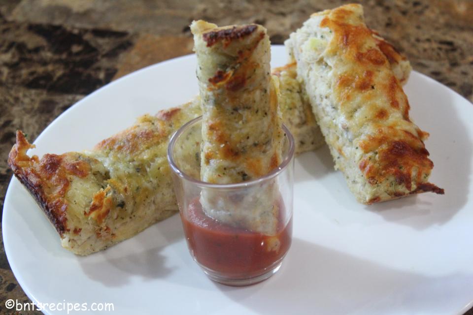 cheesy garlic breadsticks with one dipped in a small glass filled with marinara sauce on white plate on granite counter