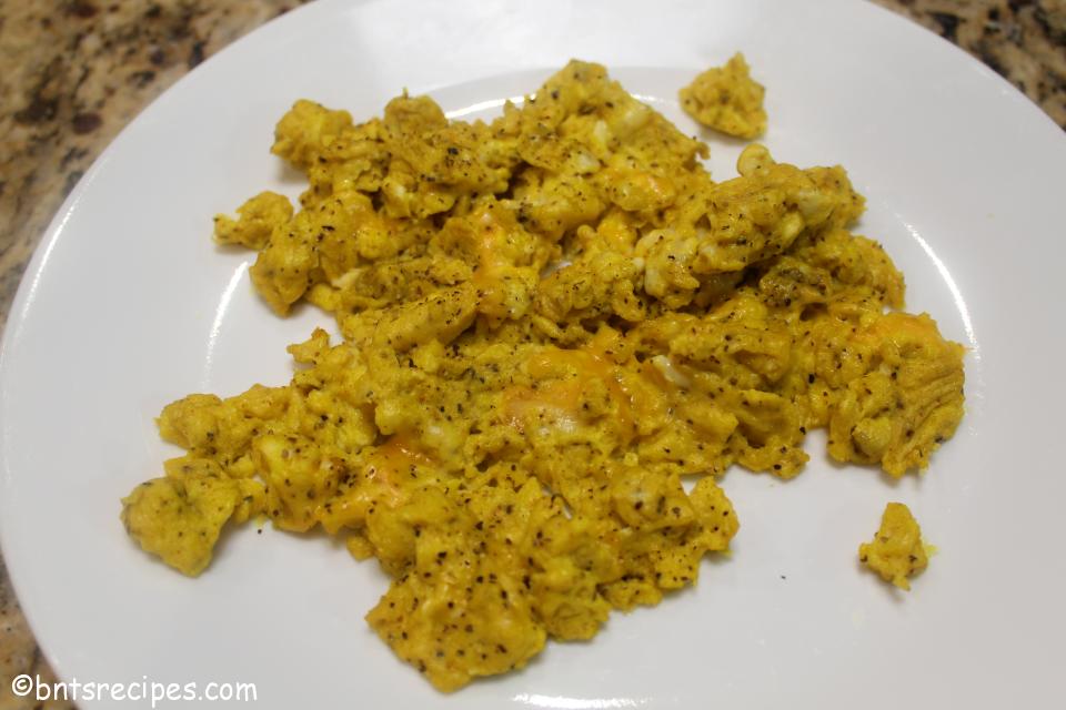 scrambled eggs with cheese and extra pepper on a white plate
