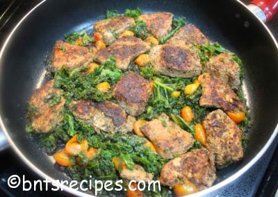 aerial view of jerked chicken, kale, and cherry tomatoes in large red skillet