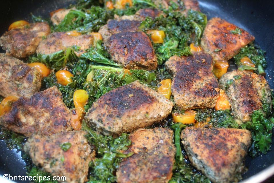 close-up view of jerked chicken, kale, and cherry tomatoes in large red skillet