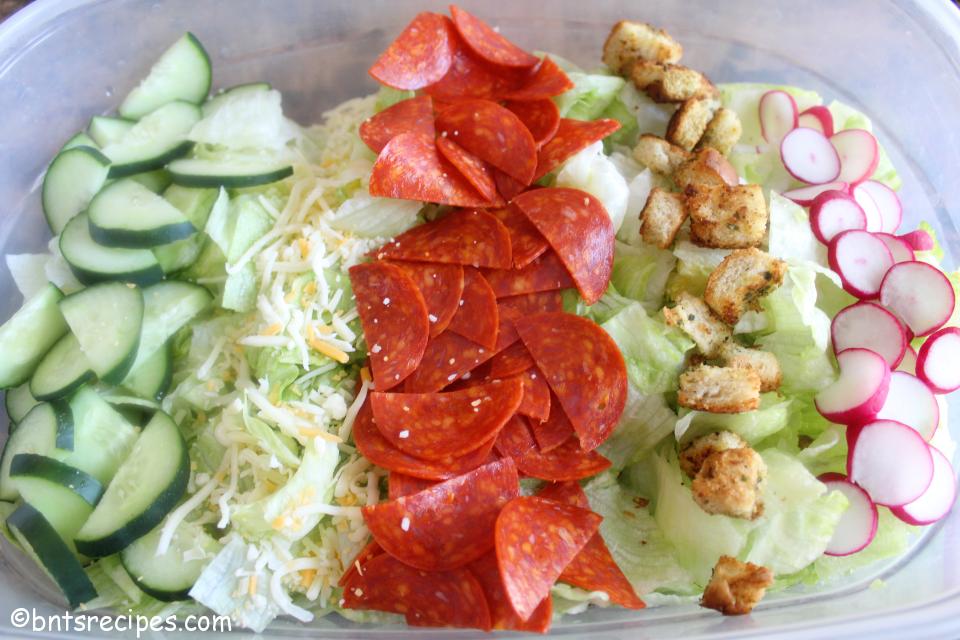 aerial view of layered Italian iceberg lettuce salad with cucumbers, shredded cheese, pepperoni, croutons, and radishes