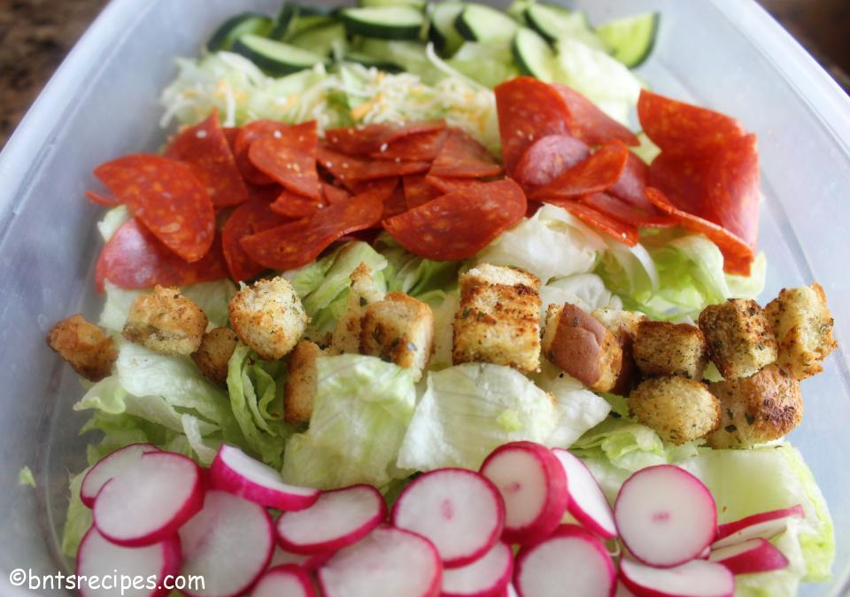 close-up of layered Italian iceberg lettuce salad with cucumbers, shredded cheese, pepperoni, croutons, and radishes